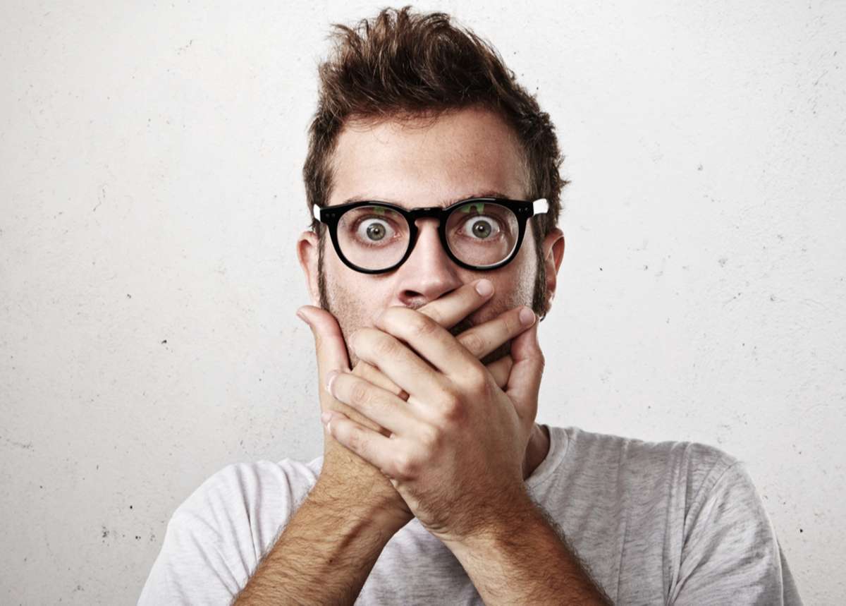 Portrait of a shocked young man covering his mouth with hands