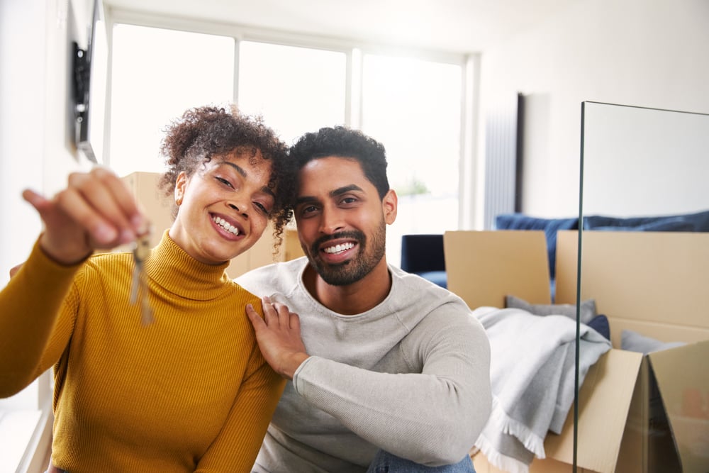 couple sitting on floor in lounge holding keys to new home